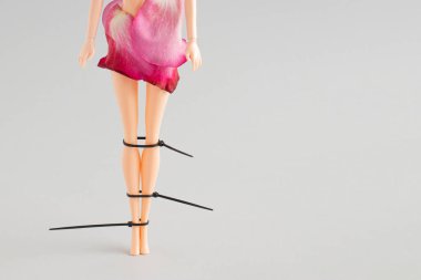 Girl doll legs tied with laces and flower petals against a gray background. Creative minimal Halloween fashion concept.