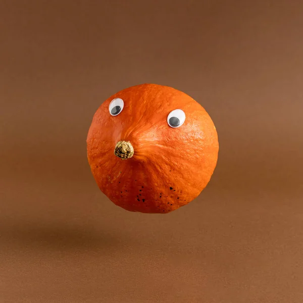 Creative layout of autumn orange pumpkin with eyes on a brown background. Creative seasonal concept.