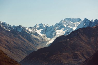 Karla kaplı tepeler ve karanlık kayalar. Dramatik manzara. Kış dağları, dağlarda kayak. Güneşli karlı tepeler. Panoramik dağ manzarası. Buzullarla kaplı kayalar ve beyaz yamaçlar.