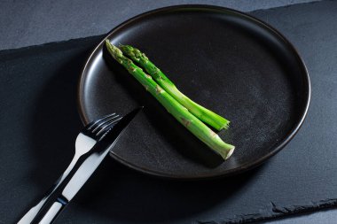 Koyu tabakta kuşkonmaz, çatal bıçak takımı taştan bir tabakta, üst tarafta.