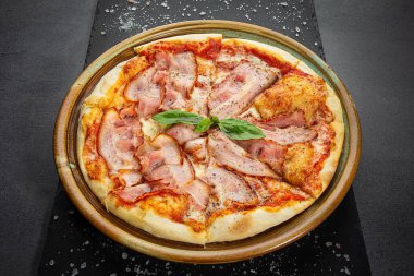 Peynir soslu İtalyan pastırmalı pizza ve kavrulmuş baharat karışımı, taş masadaki ahşap tabak..