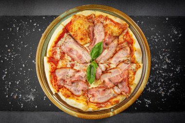 Peynir soslu İtalyan pastırmalı pizza ve kavrulmuş baharat karışımı, taş masadaki ahşap tabak..