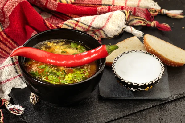 Chicken soup with vegetables in black bowl with red pepper on black background. Zeama - moldovan soup. Closeup. — Stock Photo, Image