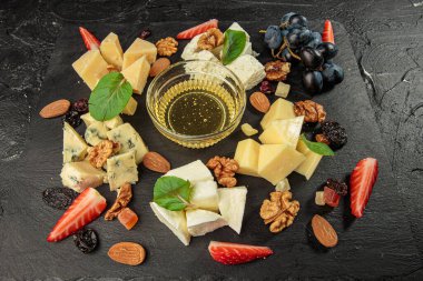 Şarküteri işleme kurulu. Peynirler, böğürtlenler ve bal siyah tahta üzerinde.