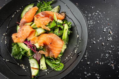 Somon dilimleri, salatalık ve avokado ile karışık yeşil salata.