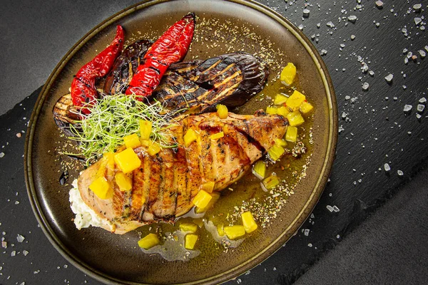 Grilled chicken breast with pineapple and grilled vegetables. A dish of authors cuisine on a dark background.