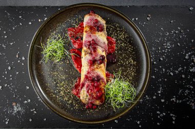 Kızarmış dolma biberin üzerine konmuş kızılcık soslu fırında domuz eti, yeşil lahanayla servis edilir.