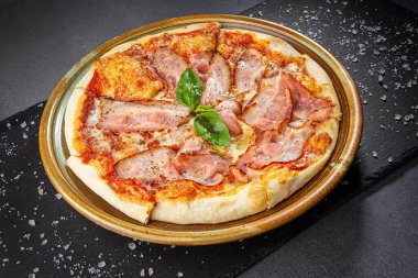 Peynir soslu İtalyan pastırmalı pizza ve kavrulmuş baharat karışımı, taş masadaki ahşap tabak..