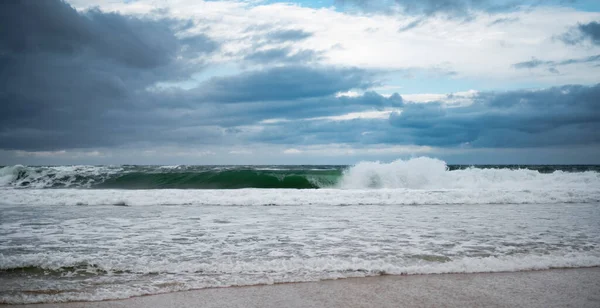 Atlantik Okyanusu kıyısına bak. Bir dalga kumlu plaja doğru koşar. Bulutlu mavi gökyüzü.