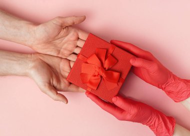 Kadın, kırmızı karton bir kutuda bir adama hediye veriyor. Kırmızı eldivenli kadın. Eldivensiz erkek eli..