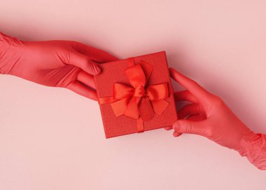 Kırmızı bir kutuda tek elli bir kadına yay veren bir kadın. Kauçuk eldivenli eller hediye kutusunu tutar..