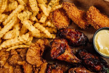 Kızarmış tavuk, patates kızartması ve ahşap tepside sos.