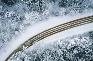 Karla kaplı köknar ağaçları ve kar fırtınasıyla çevrili güzel bir yolun büyüleyici hava manzarası.