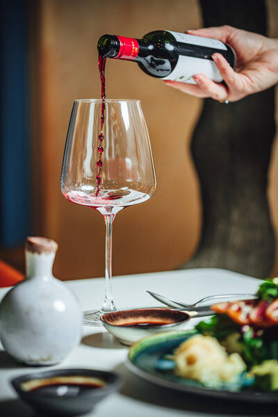 Выборочный фокус: наливание красного вина в бокал на белый стол, обеденный стол в ресторане 