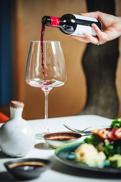 Выборочный фокус: наливание красного вина в бокал на белый стол, обеденный стол в ресторане 
