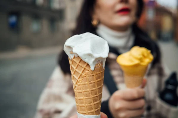 Closeup of two people holding the sweet white ice-cream cones