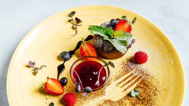 Tabağında bir kase çilek reçeli olan çikolatalı keke yakın plan.