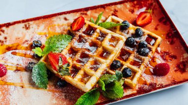 Şerbetle kaplı tatlı ve lezzetli waffle 'lar ve tabakta meyveler.