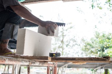 Mason tuğla kesmek için testere kullanıyor.