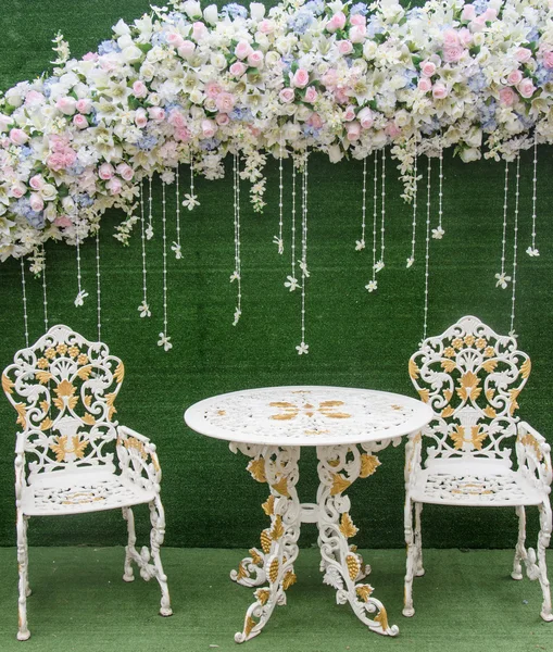 Chair and table with fowers on green backdrop — Stock Photo, Image