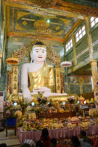 MANDALAY - JULY 31, 2015: Golden sitting Buddha decorated with flowers in temple Sagaing Hill while the faithful pray on JULY 31, 2015 in Mandalay, Myanmar — Stock Photo, Image