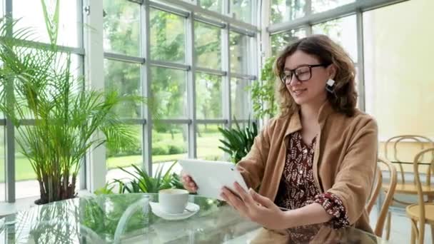 Темноволосая привлекательная деловая леди в очках и современных серьгах использует цифровой сенсорный экран в кафе — стоковое видео