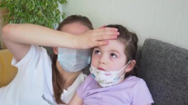 Anne ve kız tıbbi maske takıyor, alnına dokunup evde ısıyı ölçüyor..
