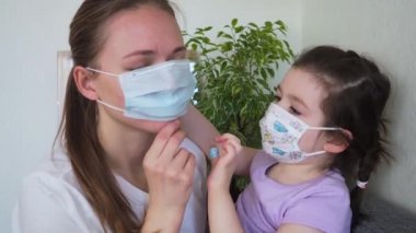 Çocuk, annenin evde tıbbi maske takmasına yardım ediyor. Coronavirus COVID-19 kavramı