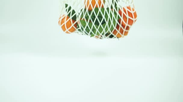 Bílý sáček z opakovaně použitelných potravinářských sítí s mandarinkami a zelenými listy, postavený na bílém podkladu na stole. Koncept ochrany přírody, opětovného použití a recyklace, produkty. — Stock video