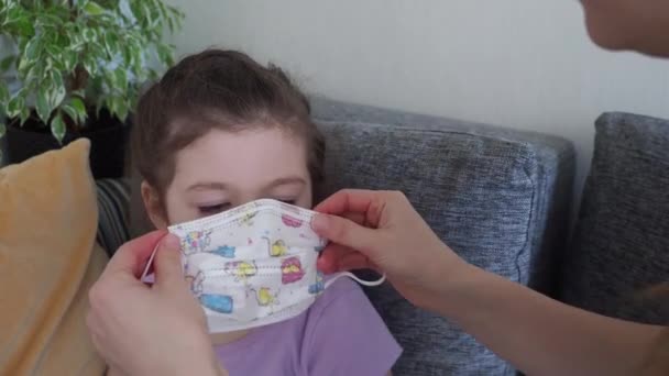 Matka pomaga córce nosić maskę medyczną podczas kwarantanny domowej. COVID-19 merów — Wideo stockowe
