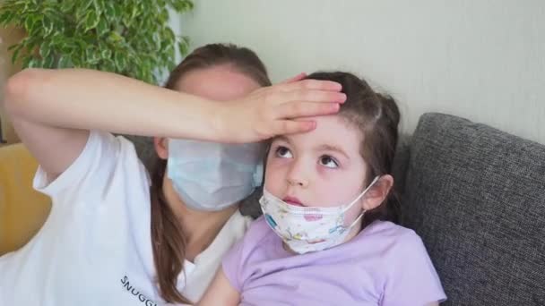 Matka a dívka nosí lékařskou masku, dotek čelo kontrolu teploty doma. — Stock video