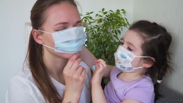 Kind helpt moeder om thuis een medisch masker te dragen. Concept van het coronavirus COVID-19 — Stockvideo