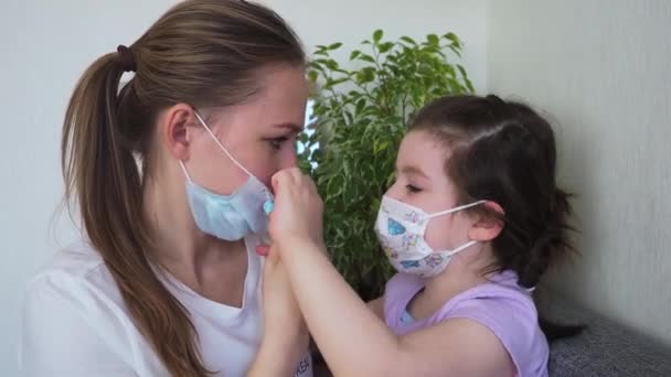 子供は母親が家で医療マスクを着るのを助ける。コロナウイルスCOVID-19の概念 — ストック動画