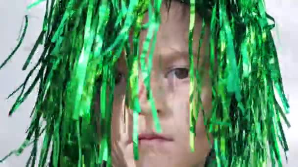 Sad girl with brown eyes and frowning eyebrows in green wig looking at the camera celebrating saint patricks day, white wall background, extreme close up — ストック動画