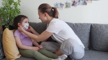 Coronavirus mers. Mother helps her cute daughter finally to put off medical mask sitting on sofa at home. Concept of coronavirus COVID-19 pandemic. Happy life after quarantine.