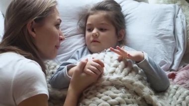 Ciddi, sevimli, anaokulu öğrencisi küçük bir kız. Sevimli annesinin peri kuyruğu konuşmasını dinliyor. El ele tutuşuyor, gülümsüyor ve yatakta birlikte uzanıyor..
