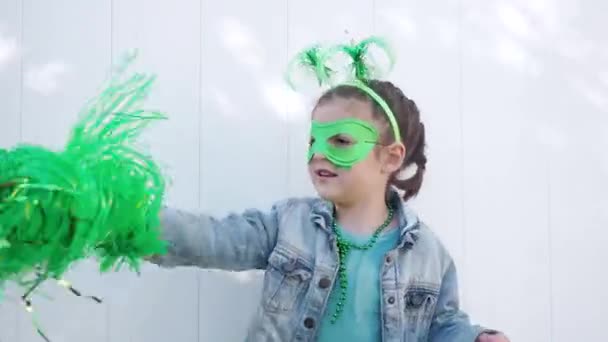 Carino felice bambino capelli castani con corna divertenti verdi, fiocco, maschera di carnevale e stella che gioca con i pon pon verdi sfondo della parete bianca, festeggiando santo patricks giorno. — Video Stock