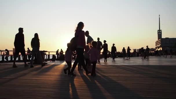 Mensen wandelen langs de promenade en genieten van gouden zonsondergang. — Stockvideo