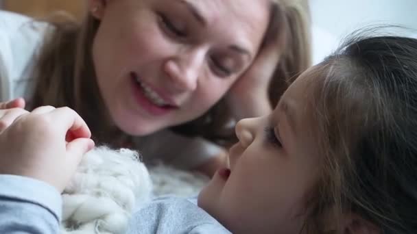 La sonriente madre le cuenta la historia a su hija pequeña. Chica enfocada. Más despacio. De cerca. — Vídeo de stock