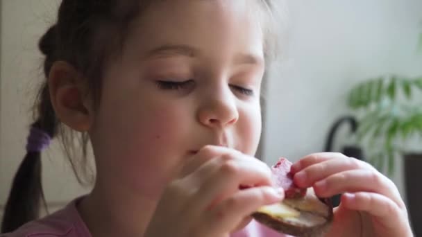 Adorable niña le gusta comer bocadillo sándwich con buen apetito. De cerca. — Vídeo de stock