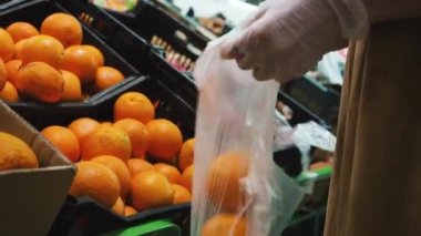 Kadın markette eldivenden portakal C vitamini seçiyor. Kapat.