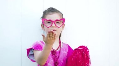 Happy kid in funny red heart glasses sending many air kisses to camera. Celebrating Valentines day. White background
