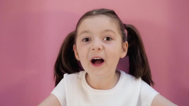 Little dark hair girl with two ponytails plays hide and seek shows different emotions. Pink background. Happy childhood — Stockvideo