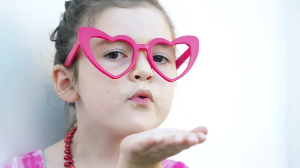 Close up. Happy dark hair and brown eyes girl in red heart glasses sends air kiss looking at the camera. Valentines day