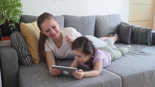 Glückliche Familienmutter und kleine Tochter mit digitalem Tablet auf dem heimischen Sofa während sozialer Distanzierung und Selbstisolierung in Quarantäne wegen Coronavirus — Stockvideo