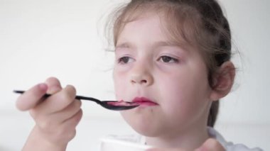 Kapatın. Sevimli koyu renk saçlı ve kahverengi gözlü çocuk siyah plastik kaşıktan organik dondurma yiyor. Beyaz arkaplan