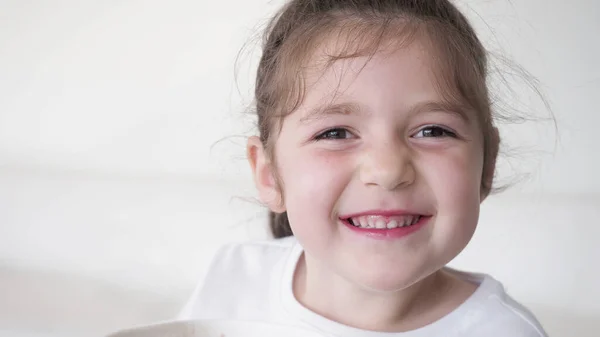 Siyah saçlı, beyaz tişörtlü, kameraya gülümseyen kahverengi gözlü çocuk. Beyaz arkaplan