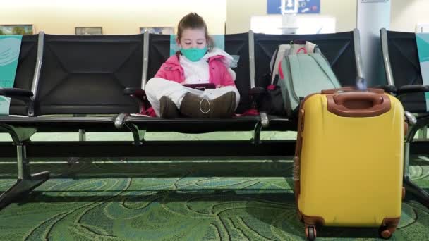 Na pandemie nieuw normaal leven - Kind zit alleen in de luchthaven check-in gebied met tablet in haar handen. — Stockvideo