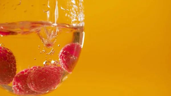 Makro aşırı yakın çekim. Ahududu, sarı arka planda beyaz şarap bardağına dökülür. Böğürtlen etrafında kabarcıklar