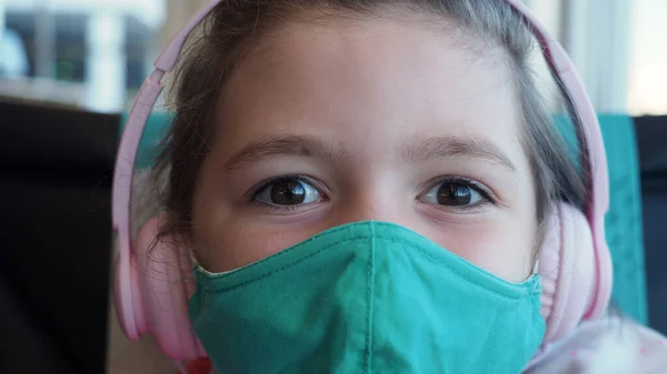 Makro, kapat. Kahverengi gözlü küçük kız yeşil maske takıyor ve pembe kulaklıklar kameraya bakıyor. Yeni gerçeklik kavramı.